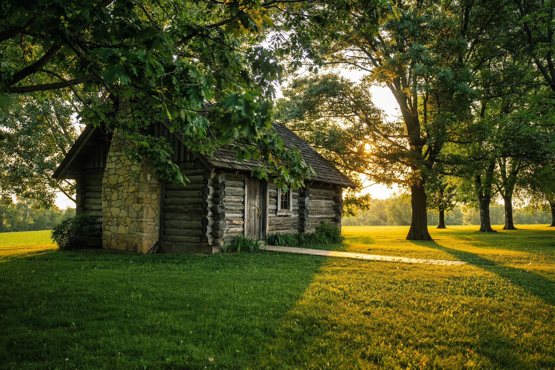 Small stone cottage in a sunlit green grove with long shadows at sunset