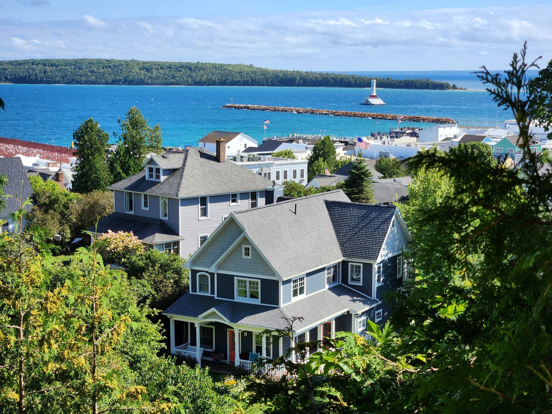 Coastal neighborhood with gray houses overlooking a blue bay and sailboats under a sunny sky