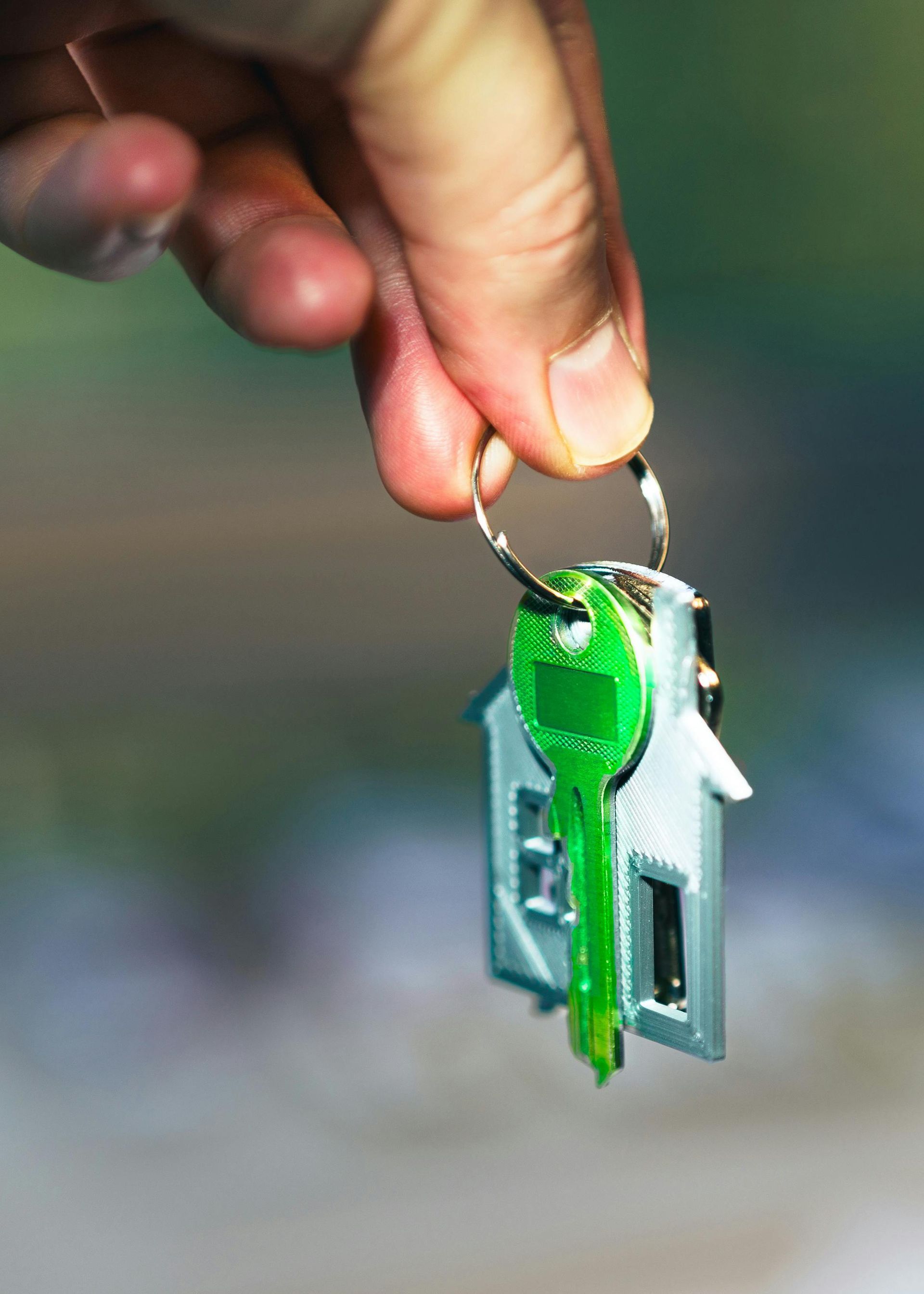 Hand holding a small house key with a green keychain