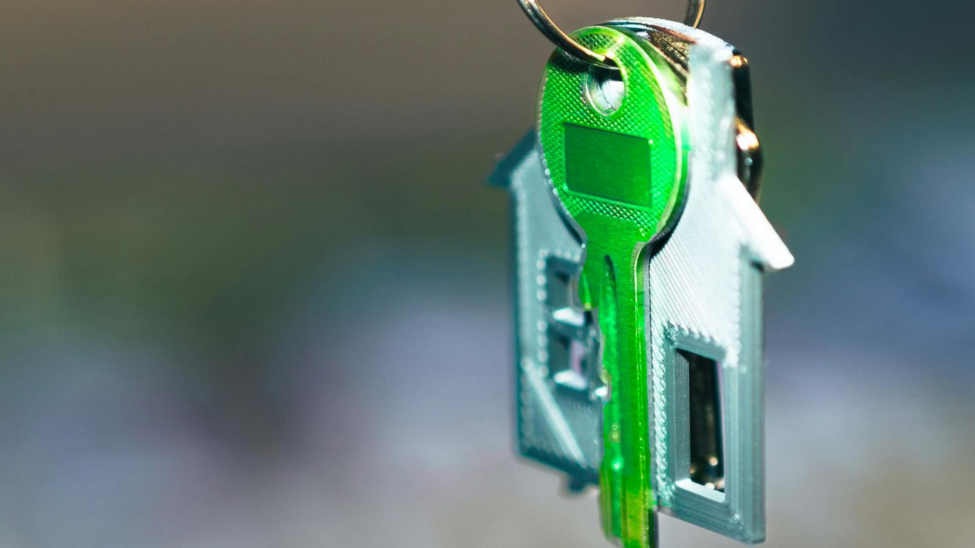 A bright green key on a keyring shaped like a miniature house.
