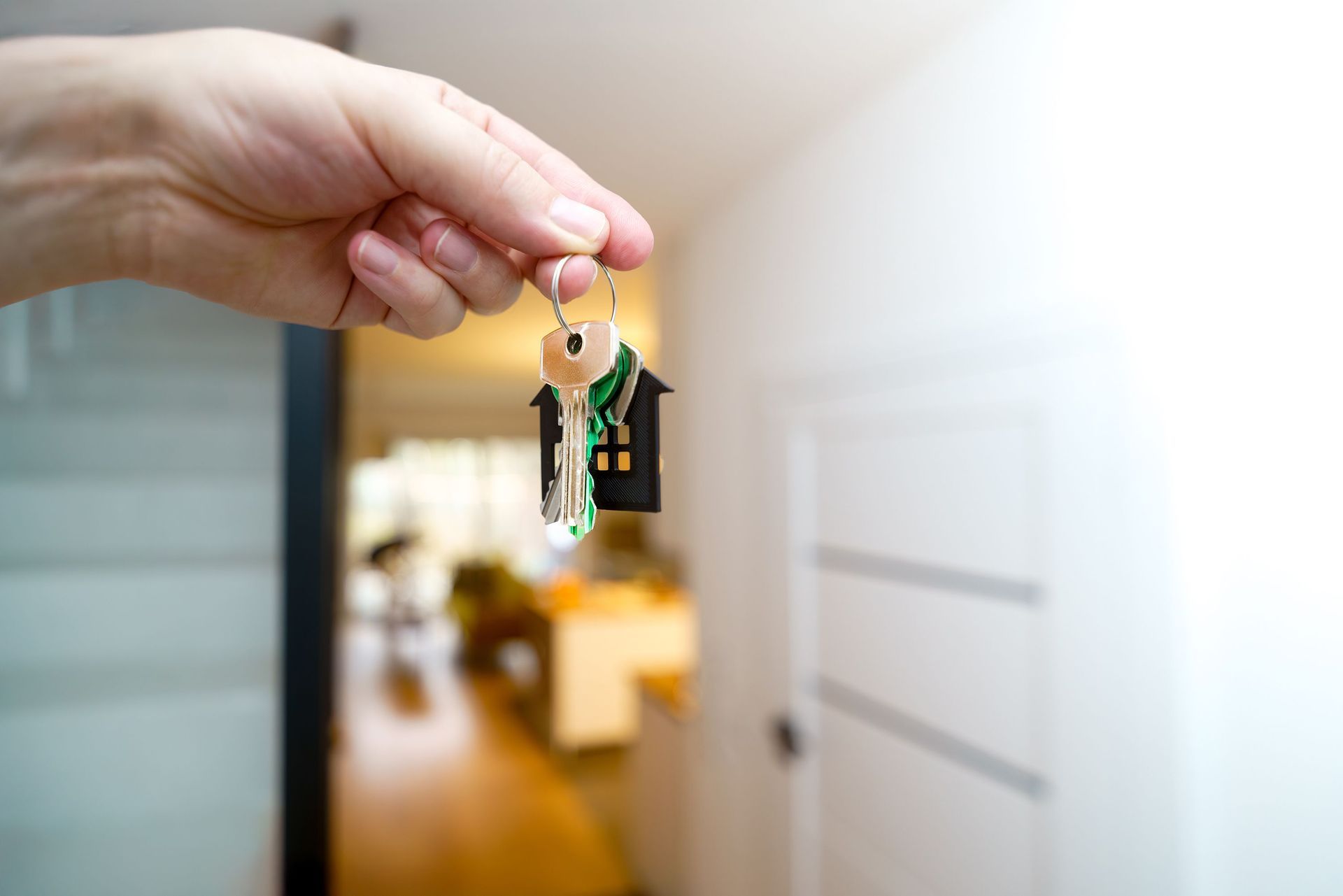 Hand holding keys in front of a softly blurred apartment door and hallway