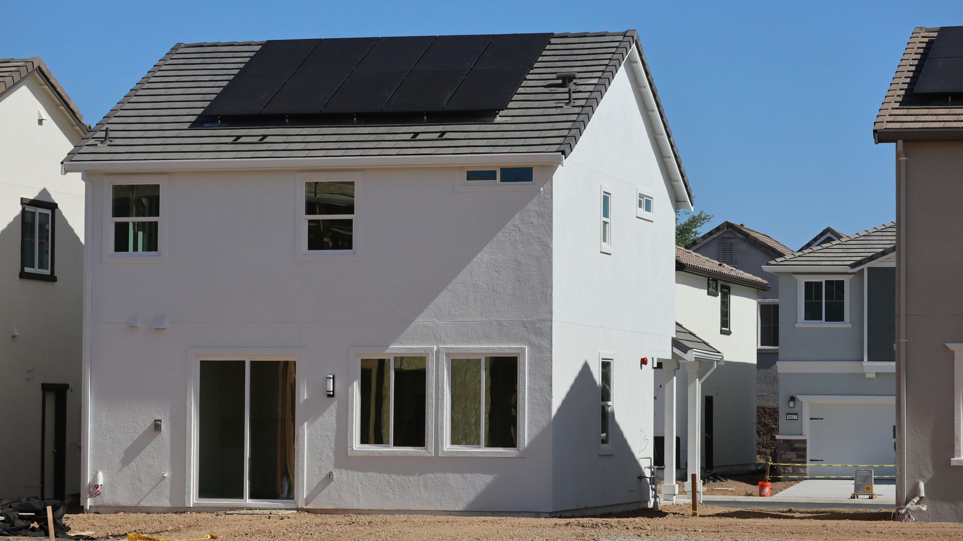 New white two-story house under construction with black roof and windows in a residential neighborhood