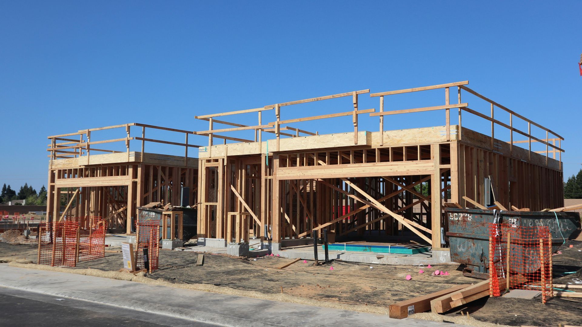 Wooden framing of two single-story residential buildings under construction on a sunny, clear-sky day.