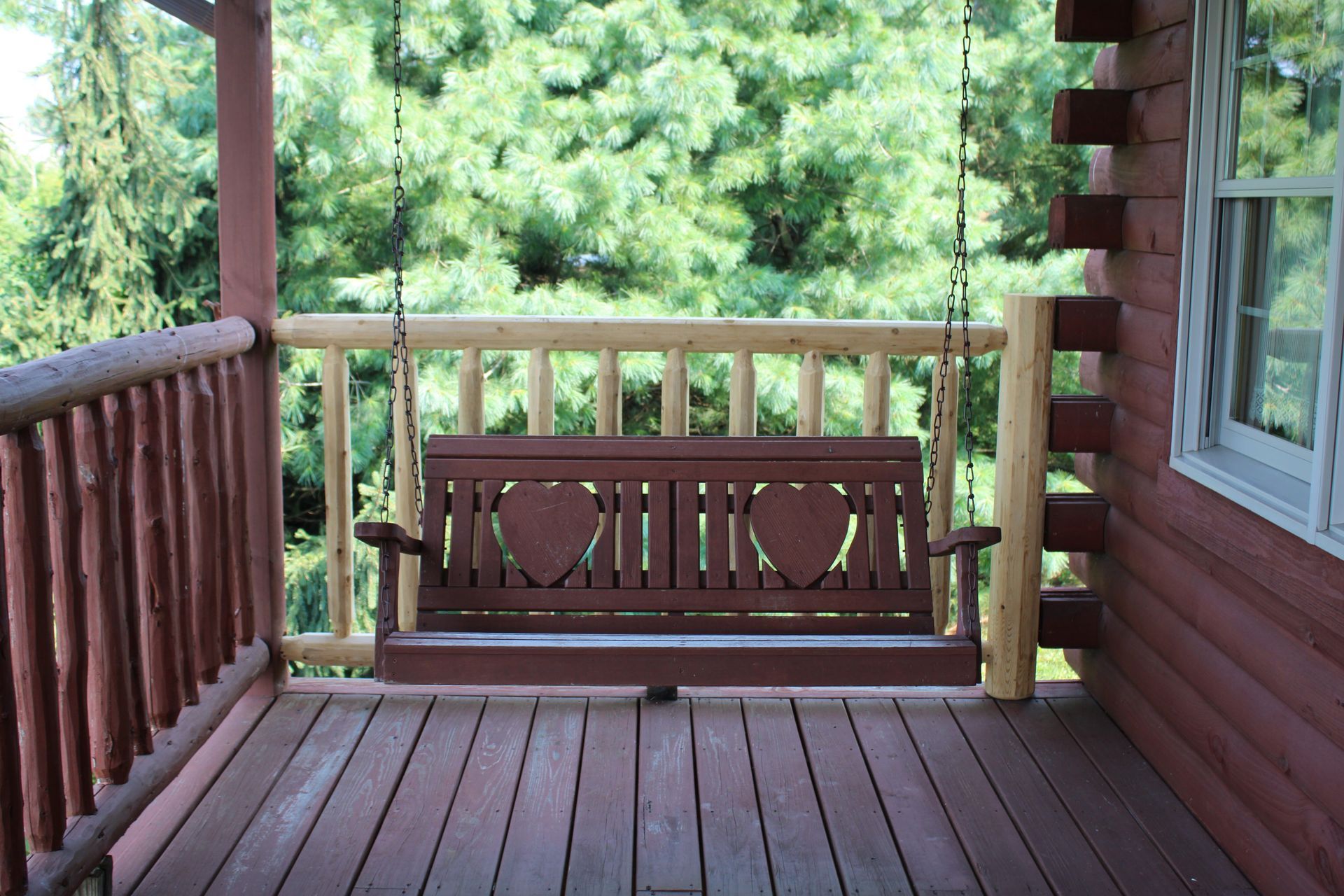 Wooden porch with a carved bench, railing, and green trees beyond the deck.
