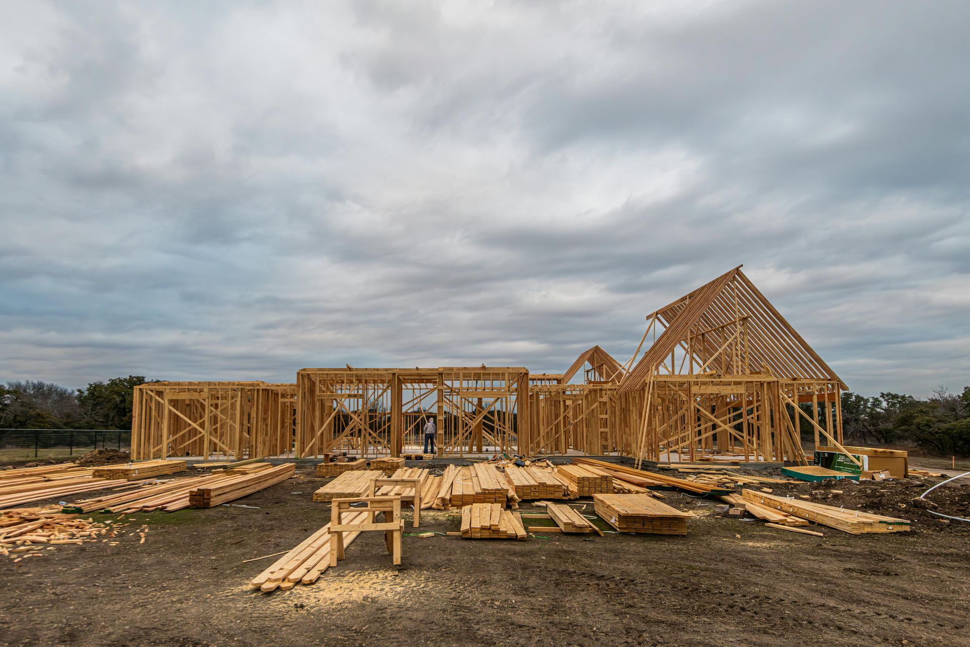 Wooden house under construction against a cloudy sky. Lumber and framing visible.