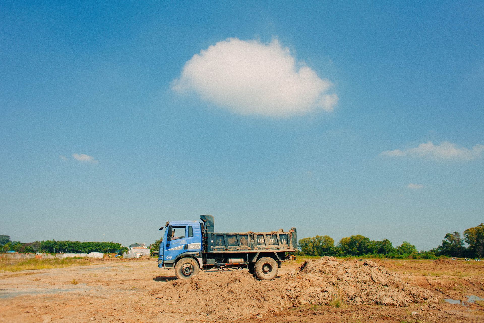Blue dump truck on a dirt construction site under a clear sky with one cloud.