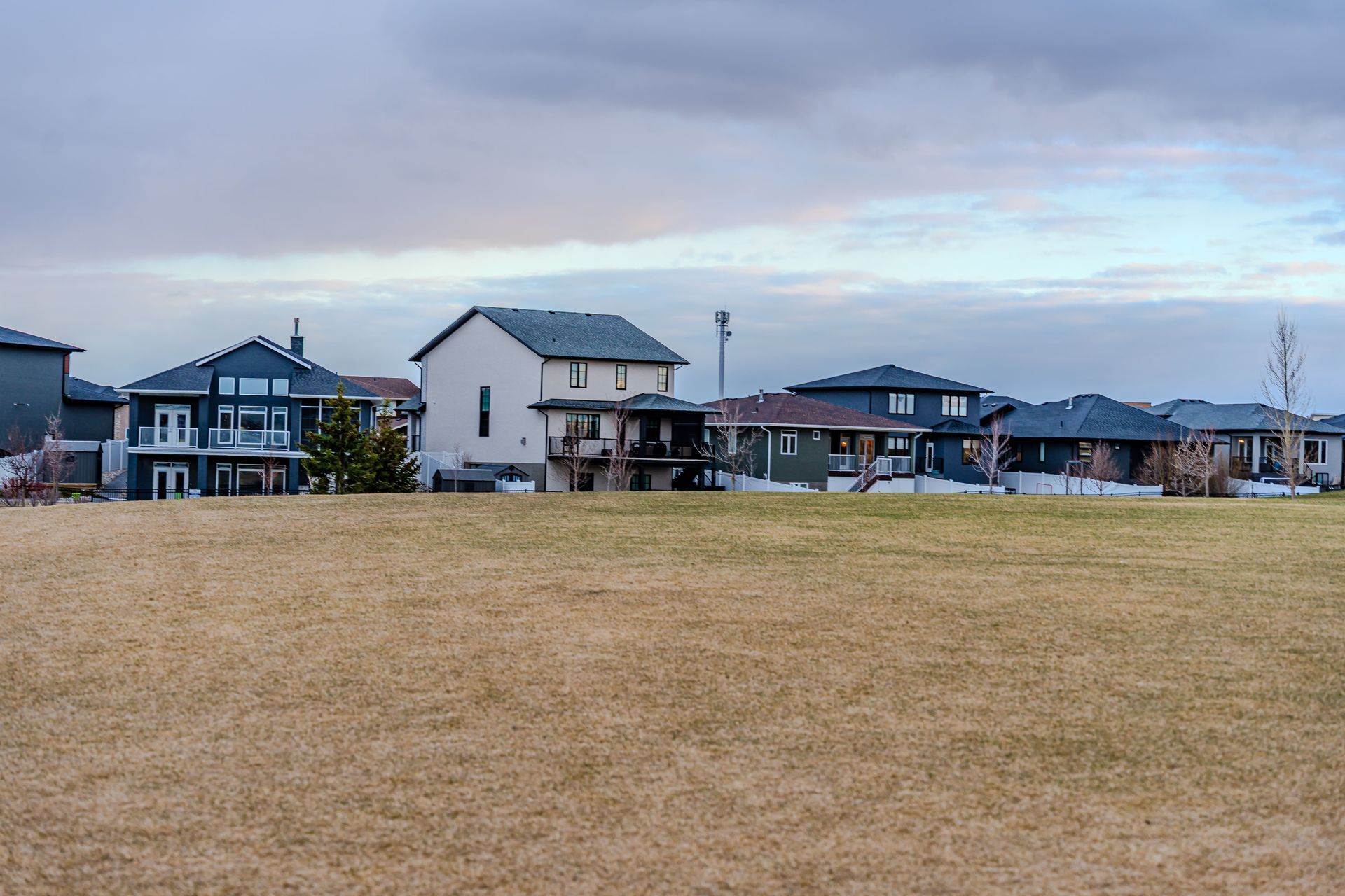 Row of suburban houses behind a wide beige field under a cloudy sky