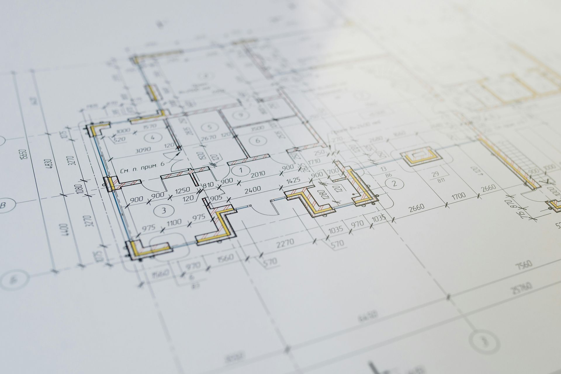 An angled, close-up view of architectural floor plan blueprints featuring black lines and faint tan accents on white paper.
