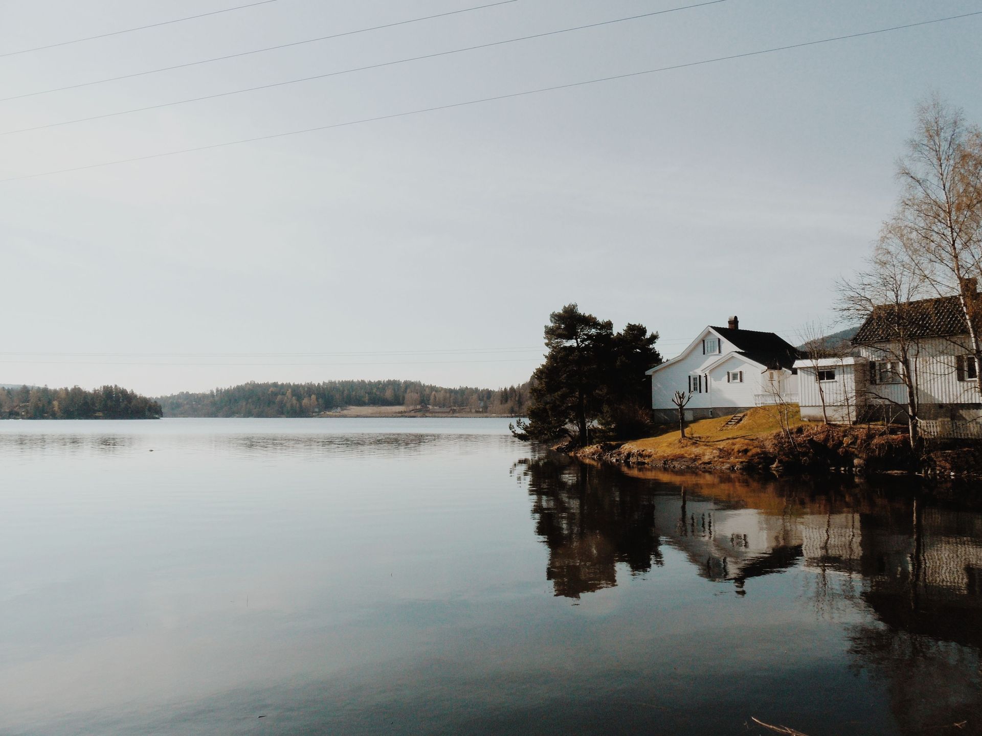 Quiet lakeside scene with a white house, bare trees, and calm water reflecting the shoreline