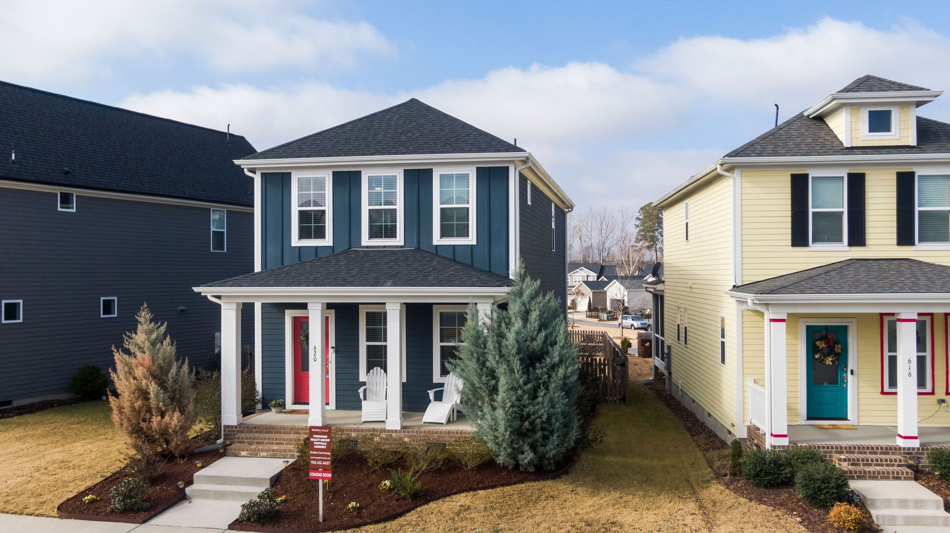 Two-story blue house with a front porch between neighboring homes in a suburban neighborhood