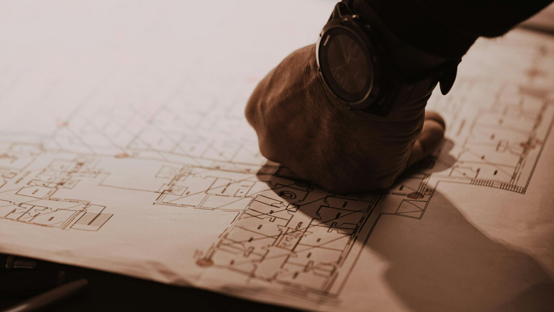 Hand on architectural blueprints, sketching building plans with a pencil