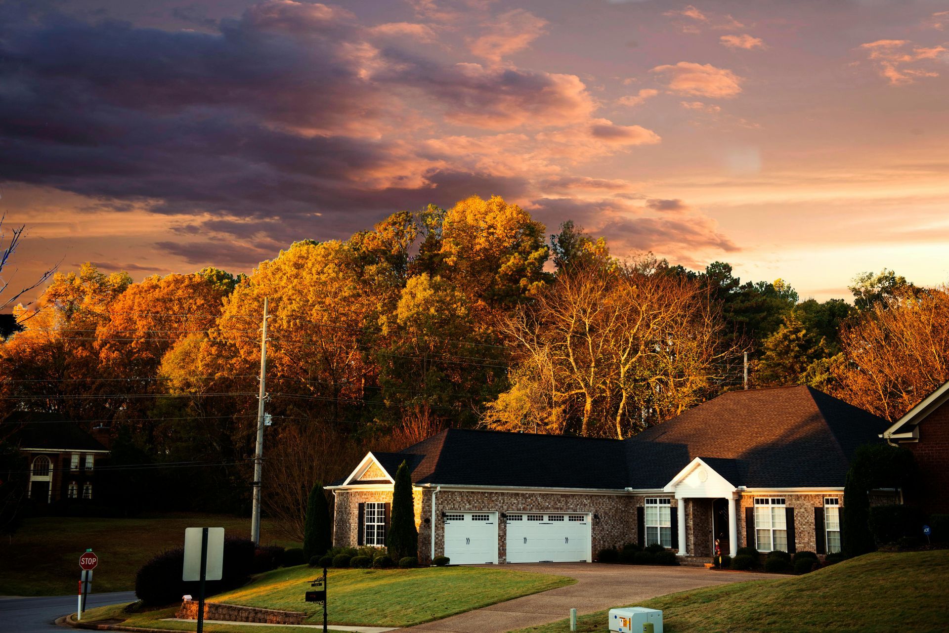 Suburban houses under a colorful sunset sky with autumn trees behind them