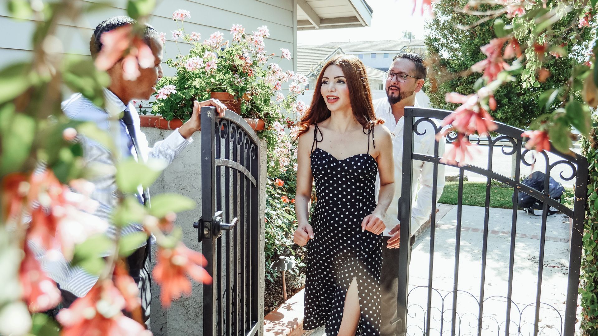 Couple entering a flower-lined gate with a greeter, outdoors in bright daylight
