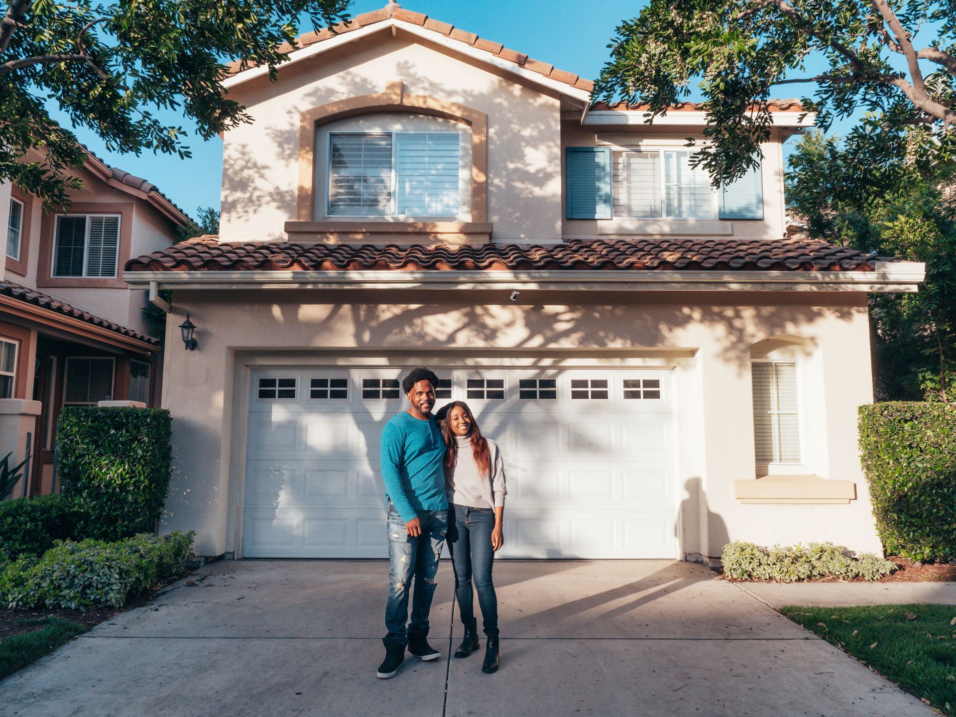 Two people standing in front of a two-car suburban house with a white garage door.