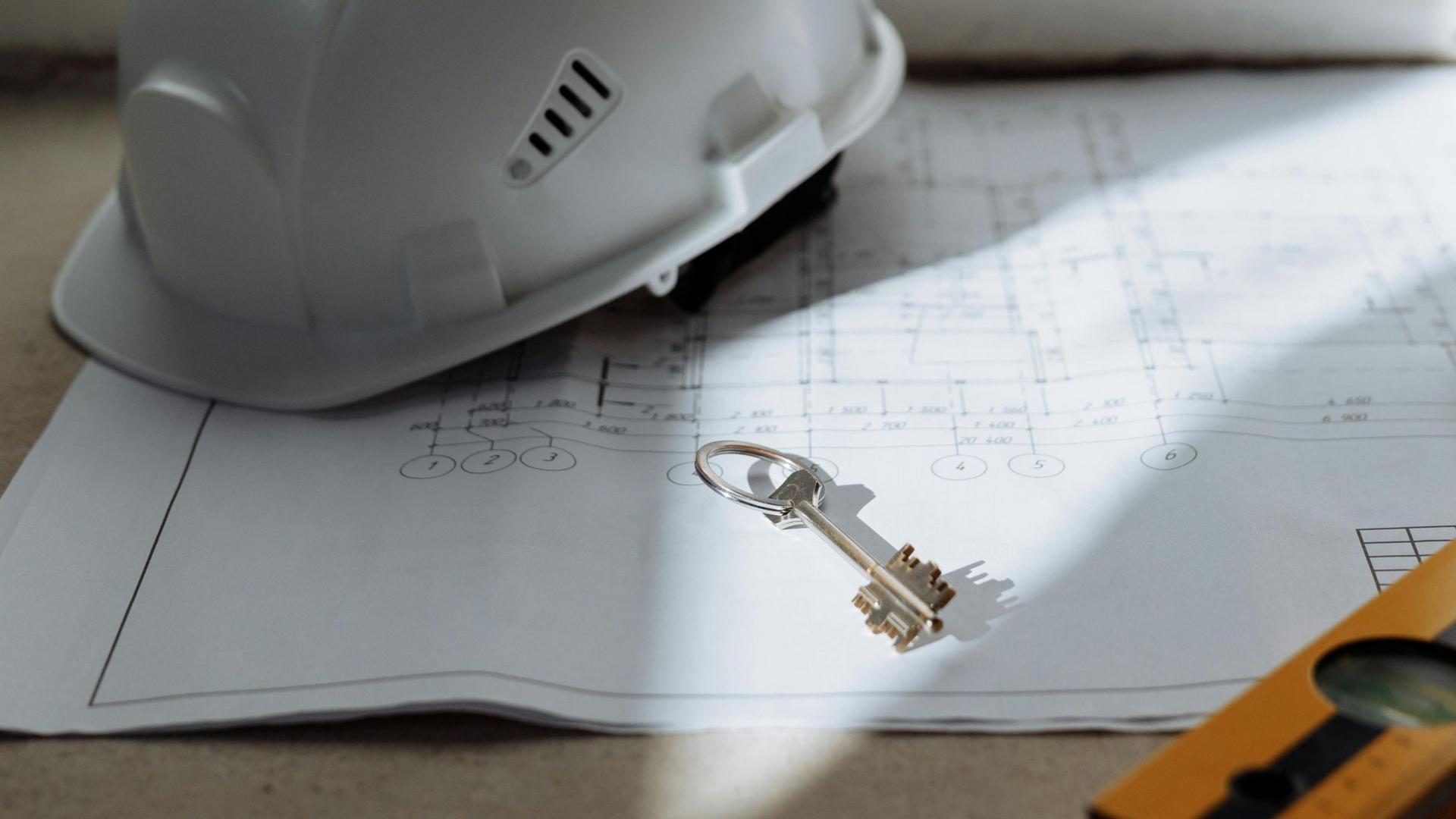 White hard hat, building plans, and a key on a desk, suggesting construction or property work