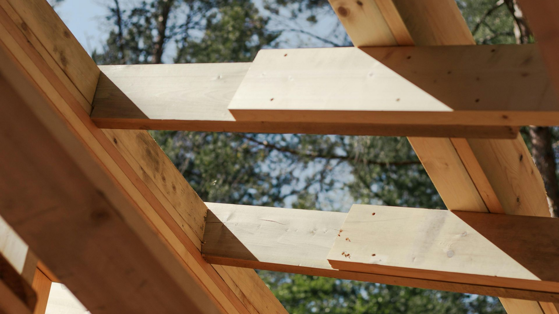 Wooden roof rafters under construction, showing joints with overlapping boards fastened together against a sky background.
