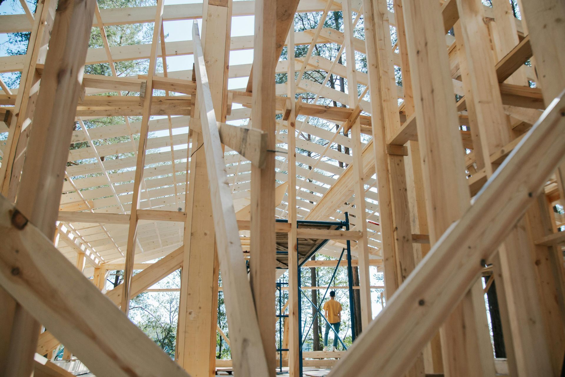 Wooden frame of a building under construction, with a person standing in the distance.
