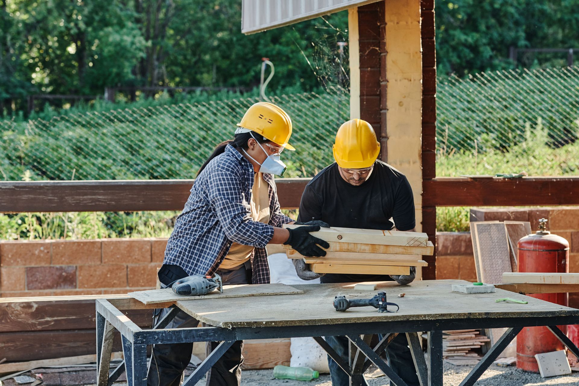 Two workers in yellow helmets assembling wood at a construction site table