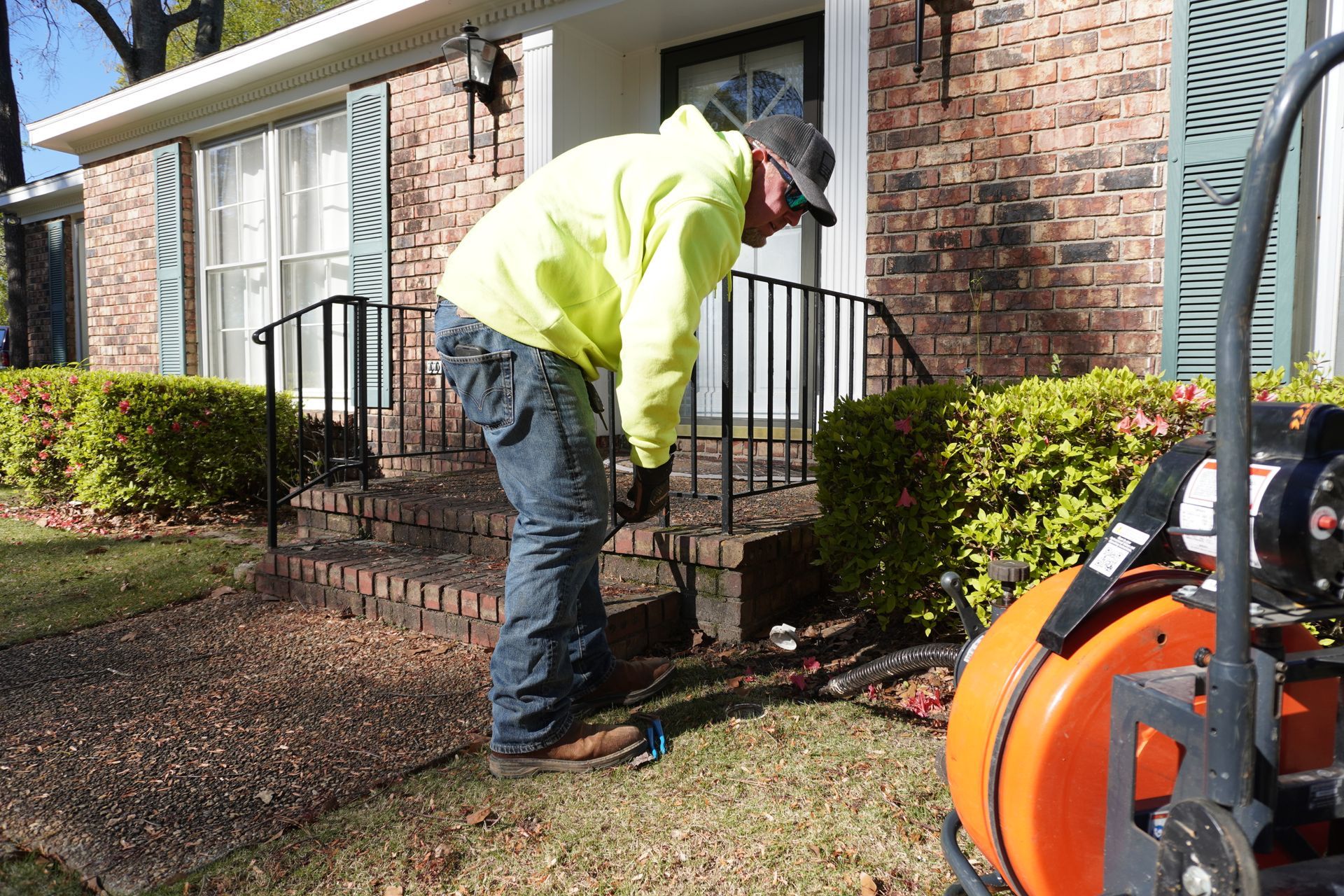 Man in neon vest working on plumbing near house steps; equipment visible.