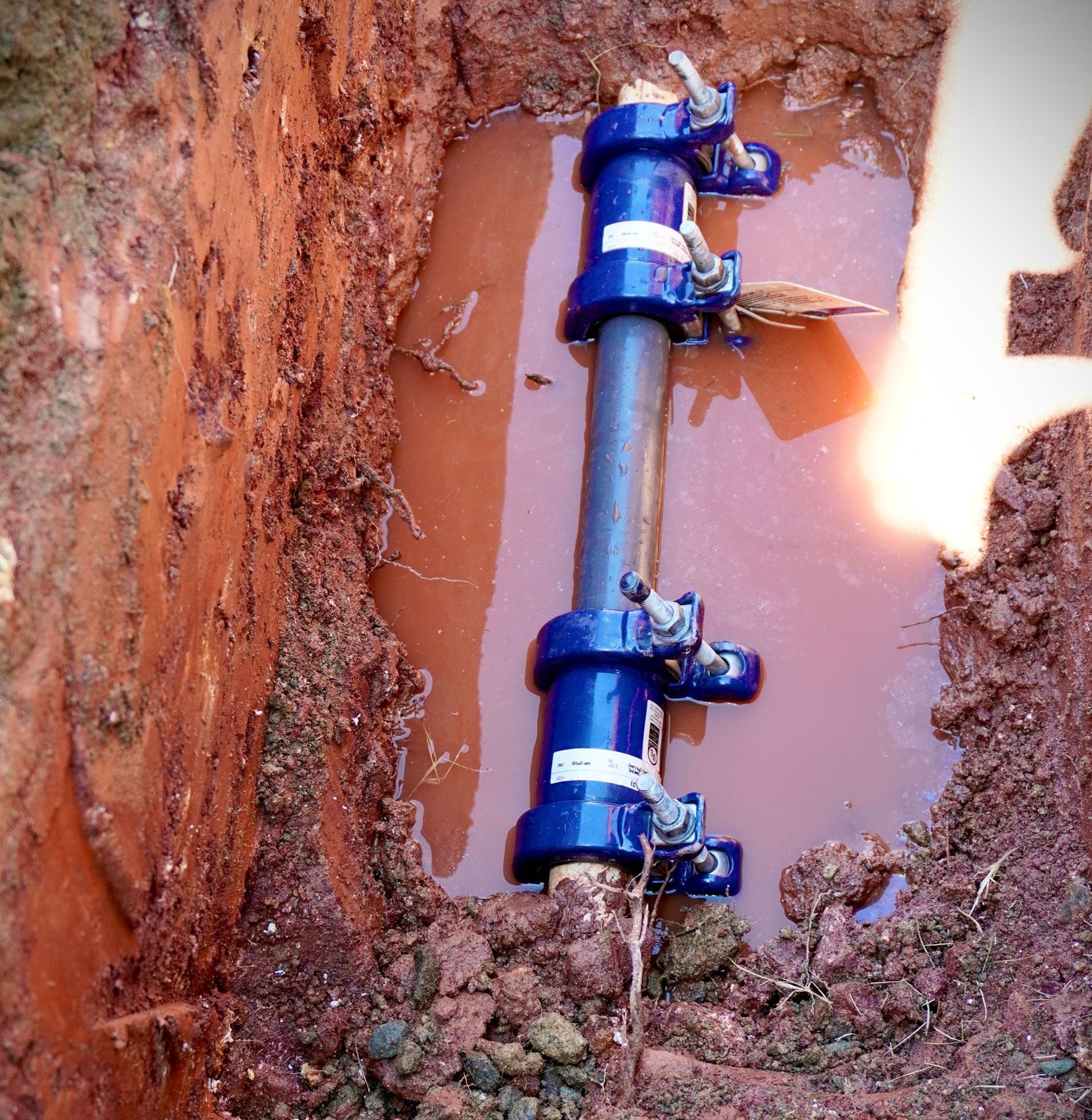 Blue pipe repair clamp in a muddy trench.