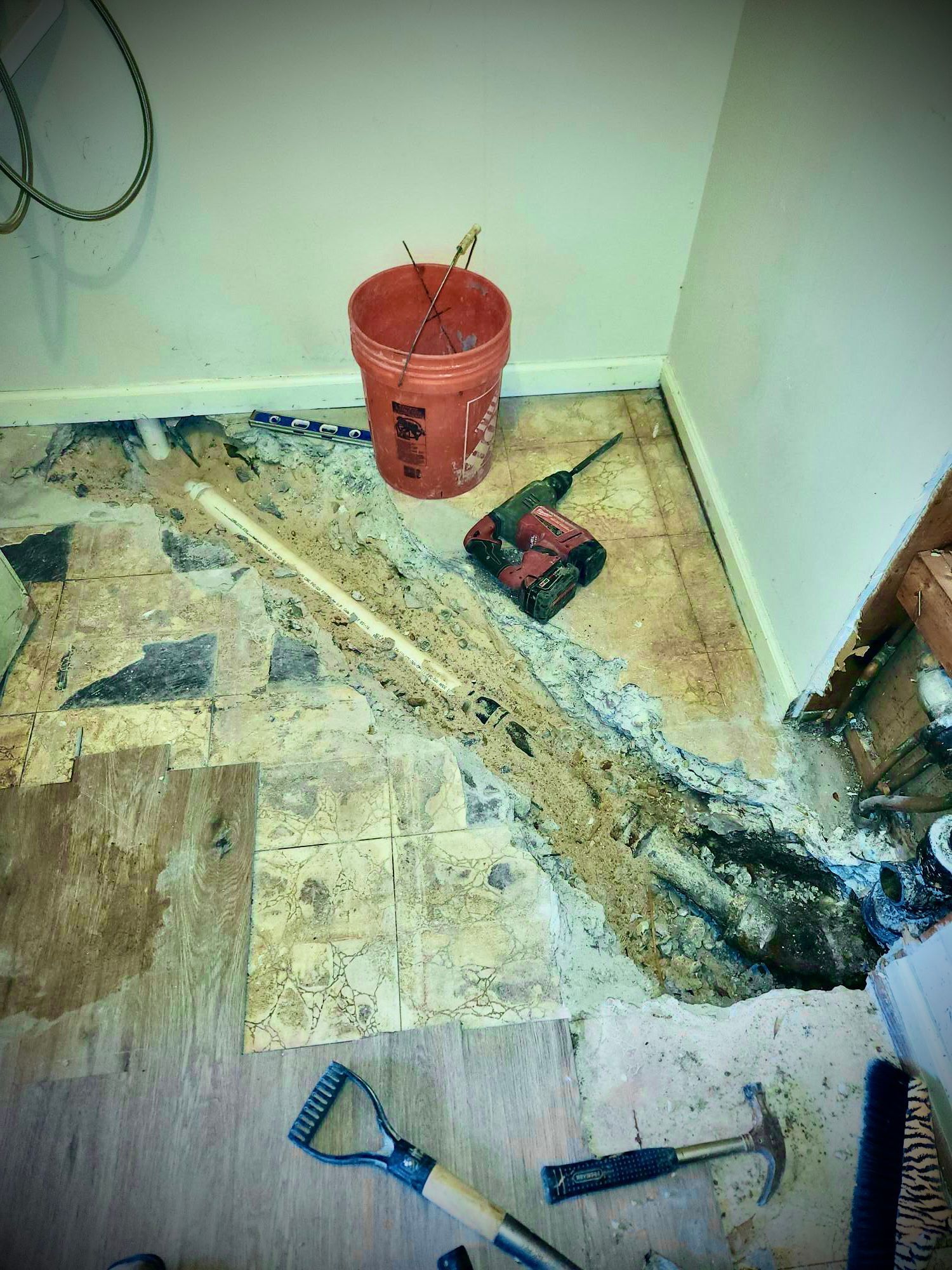 A room under construction with flooring ripped up, tools scattered, and a red bucket.