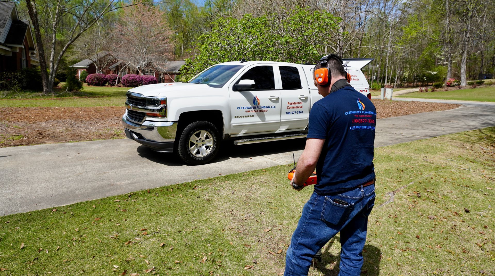 A man in blue shirt operates equipment near a white truck on a sunny lawn.