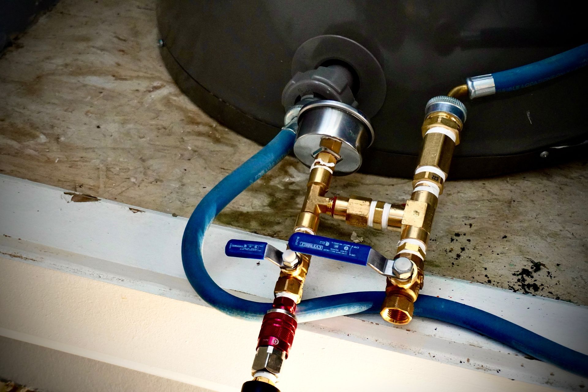 Brass plumbing fixtures connected to a dark tank, blue hoses, and valves, on a white surface.