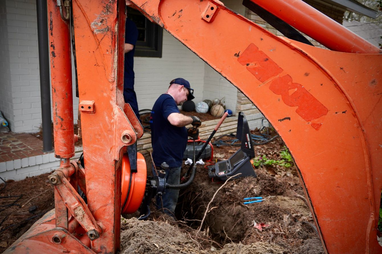 A man digging in a hole with an excavator, orange machine in front of a house.