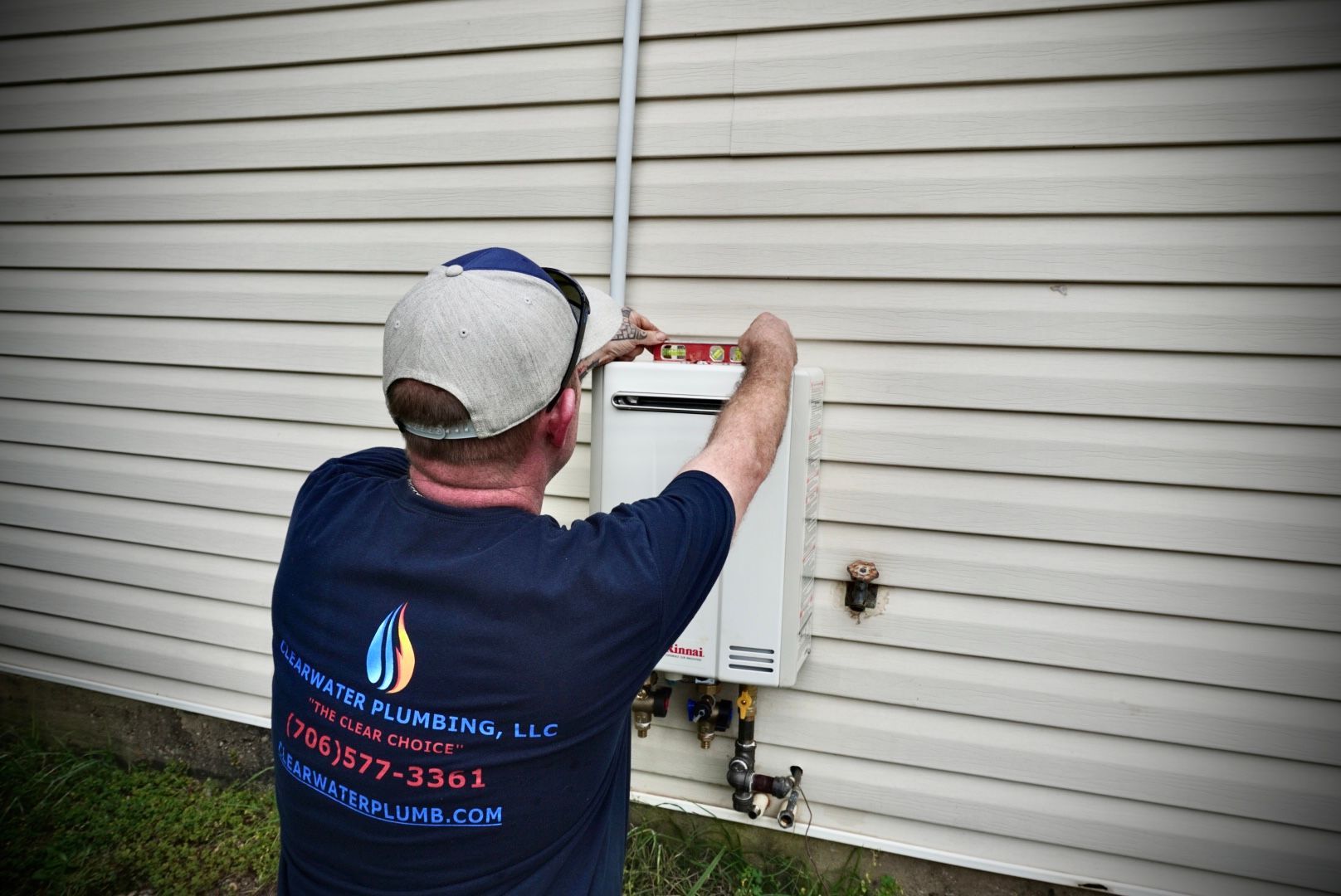 Plumber installs a water heater on the side of a house.