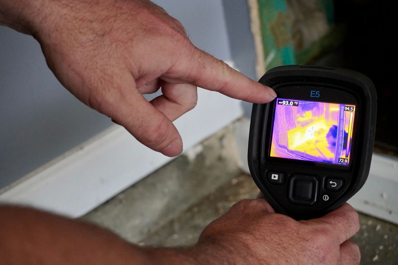 Person pointing at thermal image of a building's interior, revealing temperature variations.