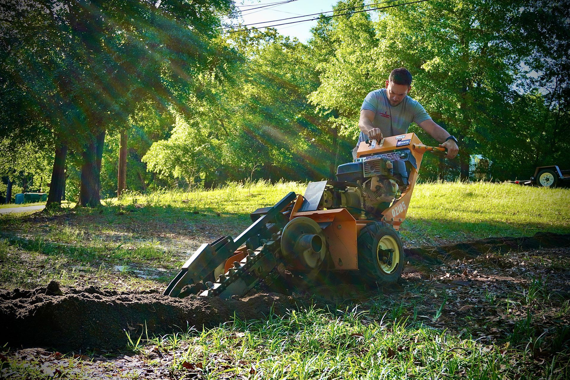 Man operating a trenching machine in a grassy area, digging a trench.