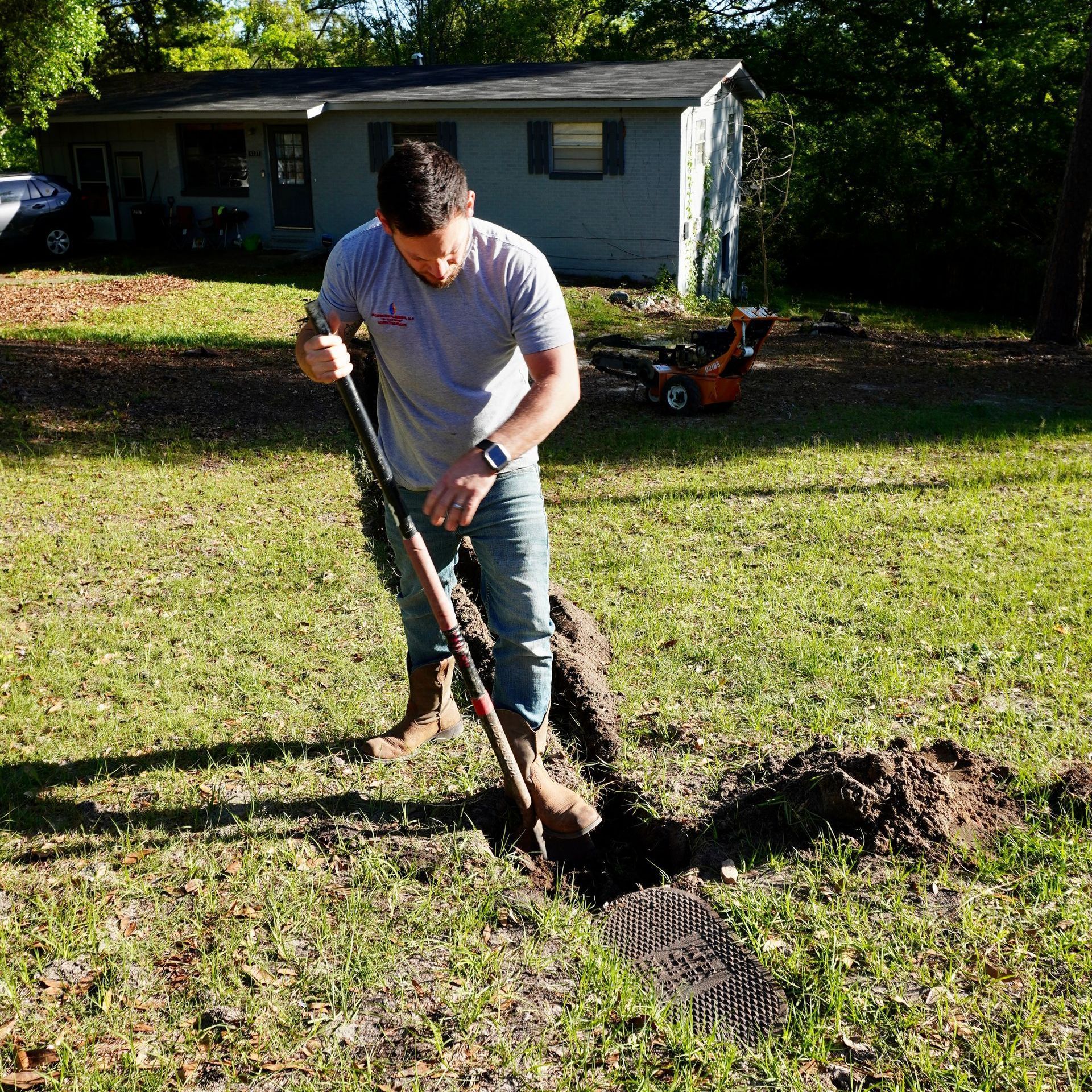 Man digging a trench in a yard with a shovel. House in background.