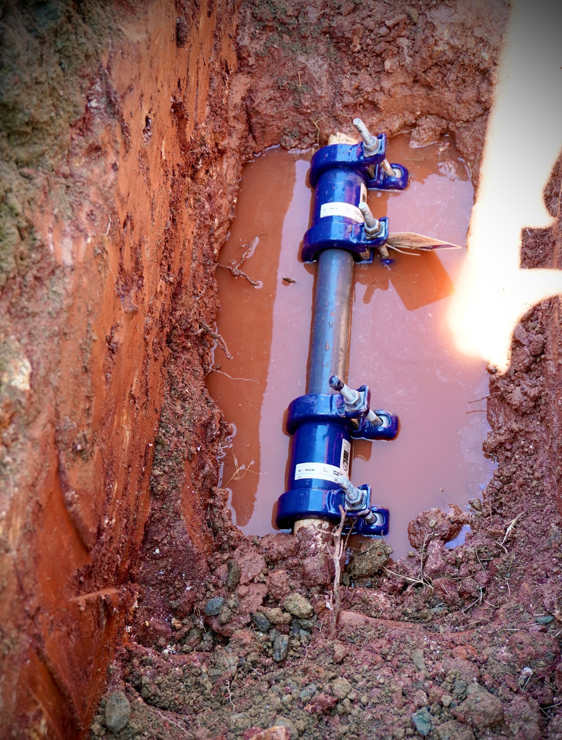Blue pipe repair equipment in a muddy trench.