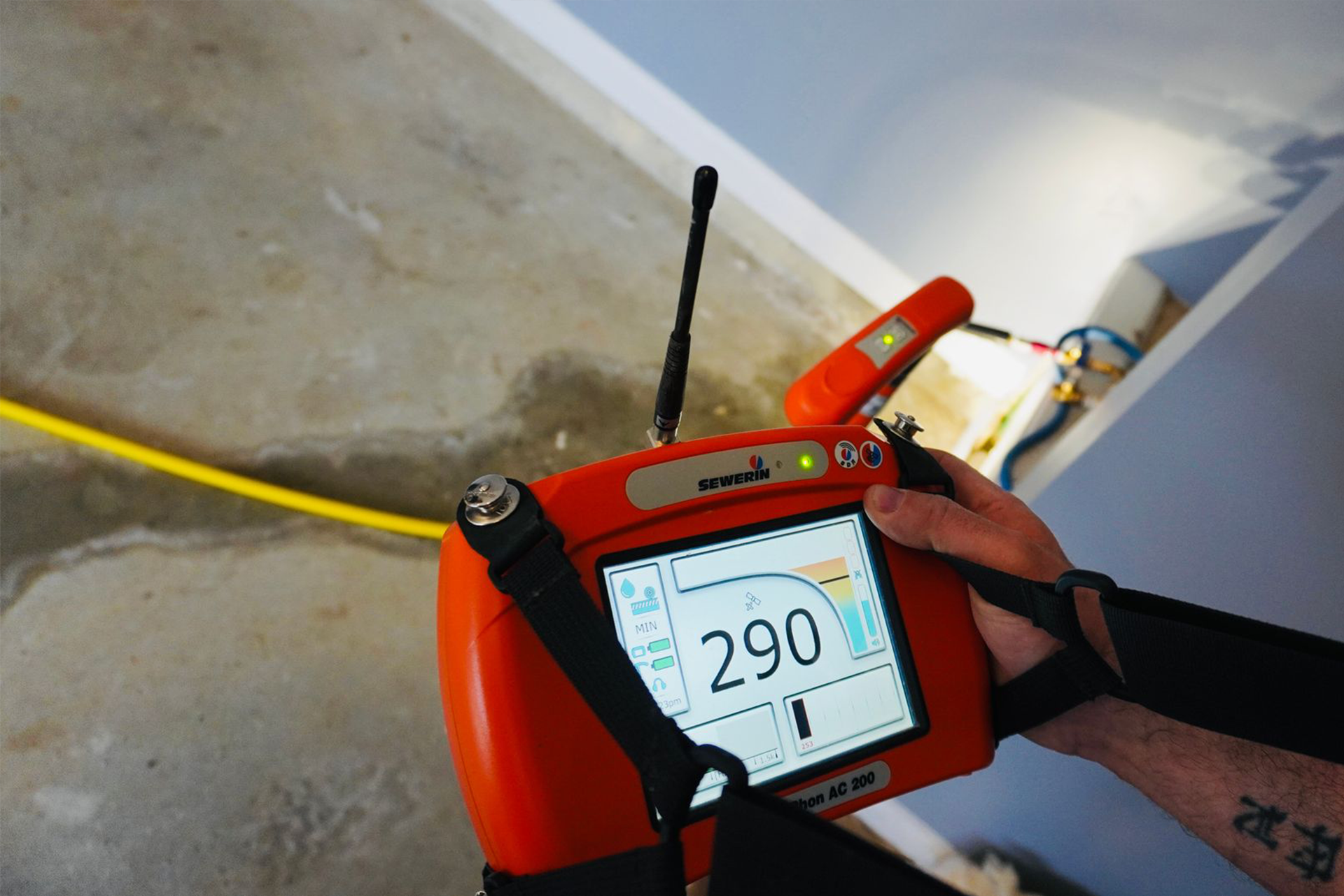 Person holding an orange device, possibly a water leak detector, in a room. The screen displays 290.