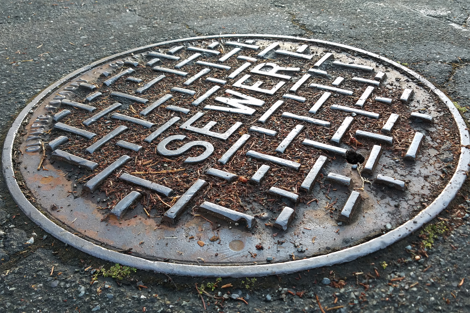 A rusty metal sewer cover on asphalt, text reads 