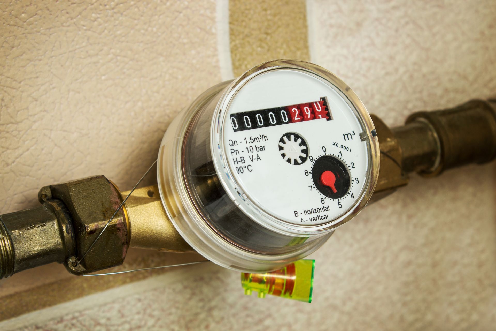 Water meter with visible numbers, connected to brass pipes, set against a beige wall.