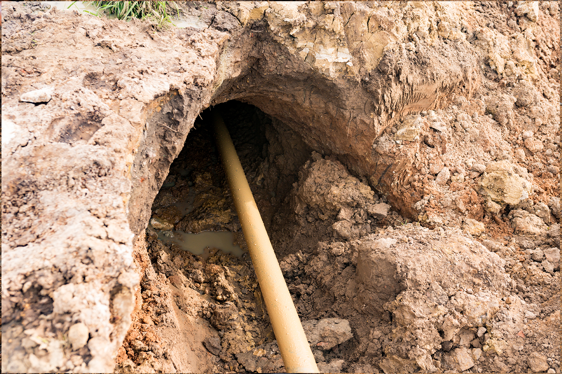 Hole in dirt with yellow pipe extending through, likely for utility work.