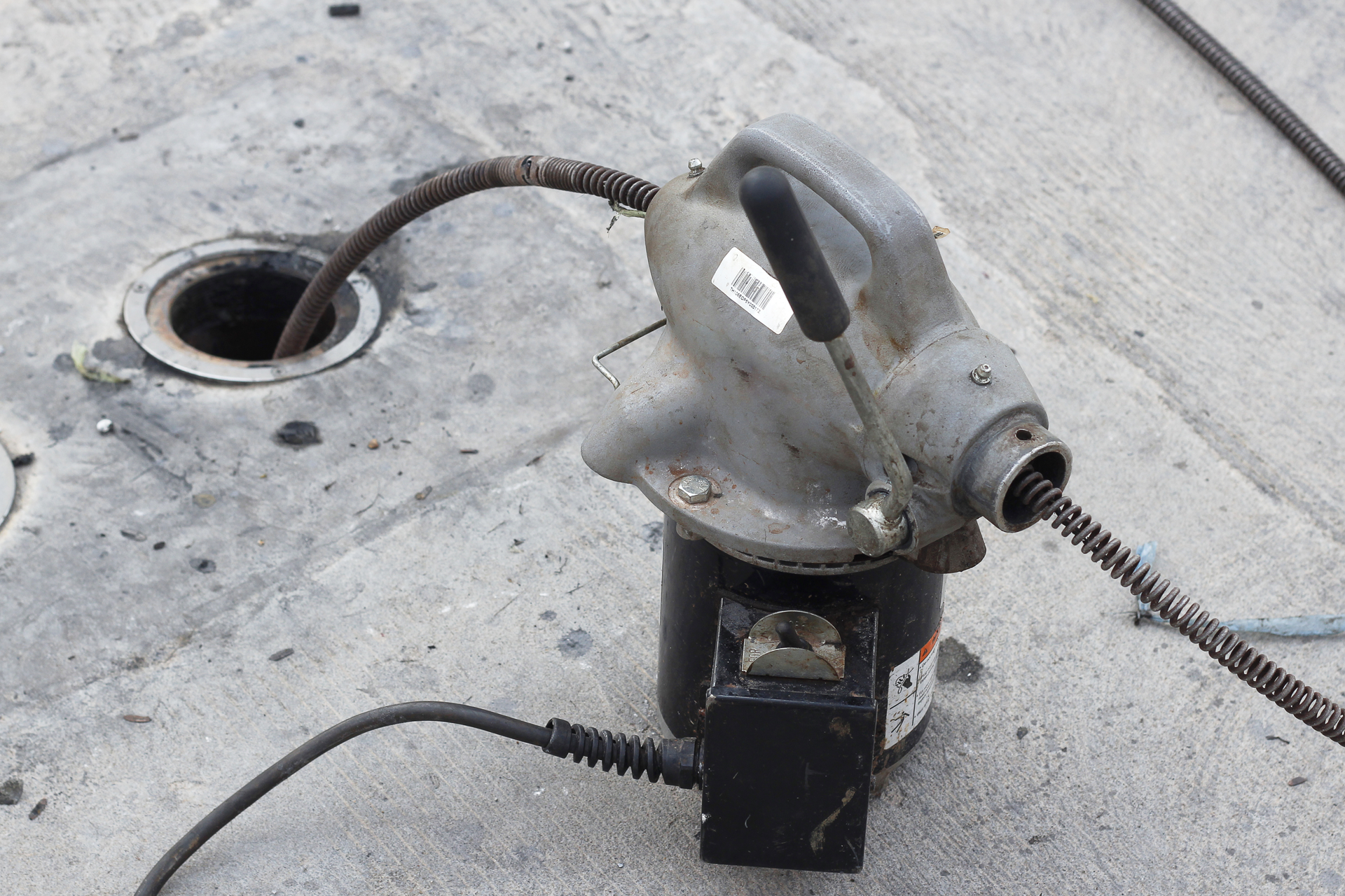 A drain cleaning machine next to an open drain, with a cable inserted into the drain.