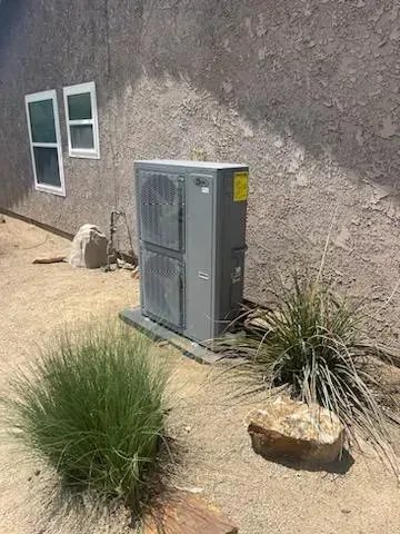 Air conditioning unit next to a stucco wall, with two windows above it.