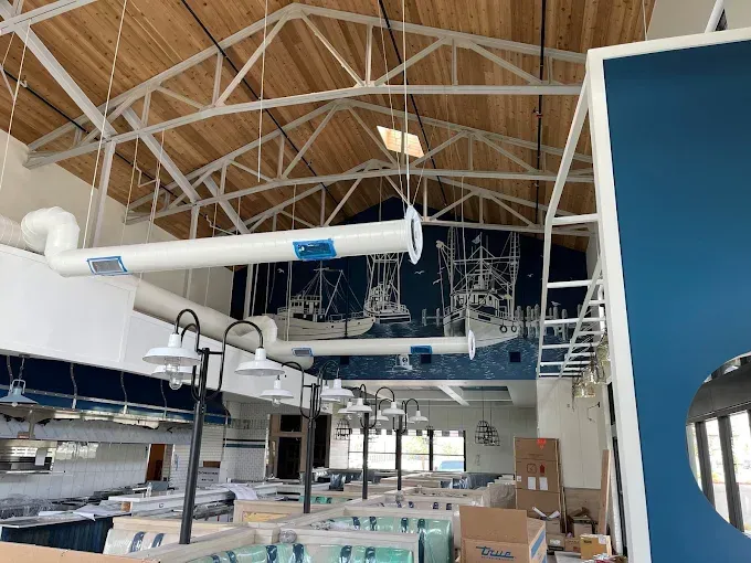 Interior of a restaurant under construction with exposed beams, ventilation, and a mural of fishing boats.