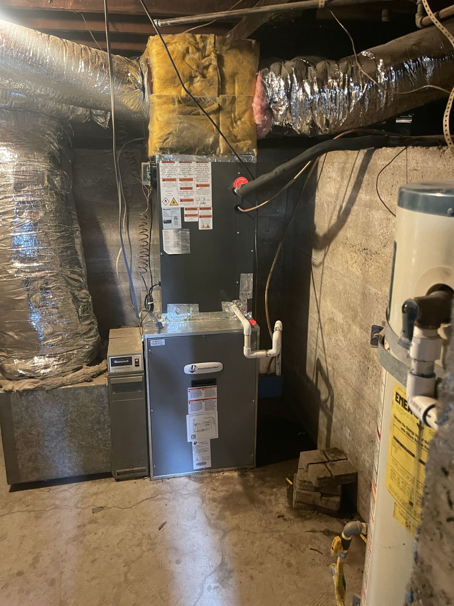 Furnace and hot water heater in a basement. Ductwork and concrete walls are visible.