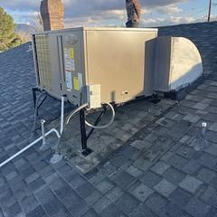 HVAC unit on a roof with a person visible. The unit is supported by metal brackets and has pipes attached.