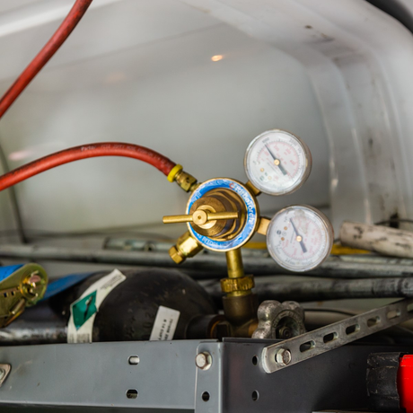 Gas regulator with gauges and red hose, mounted in a vehicle interior.