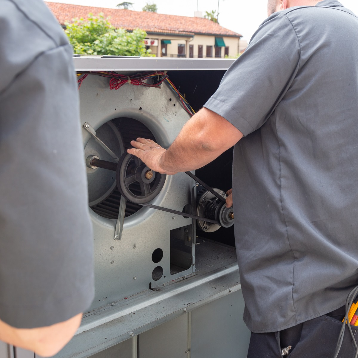Two technicians inspecting the open fan compartment of a large HVAC unit outdoors.