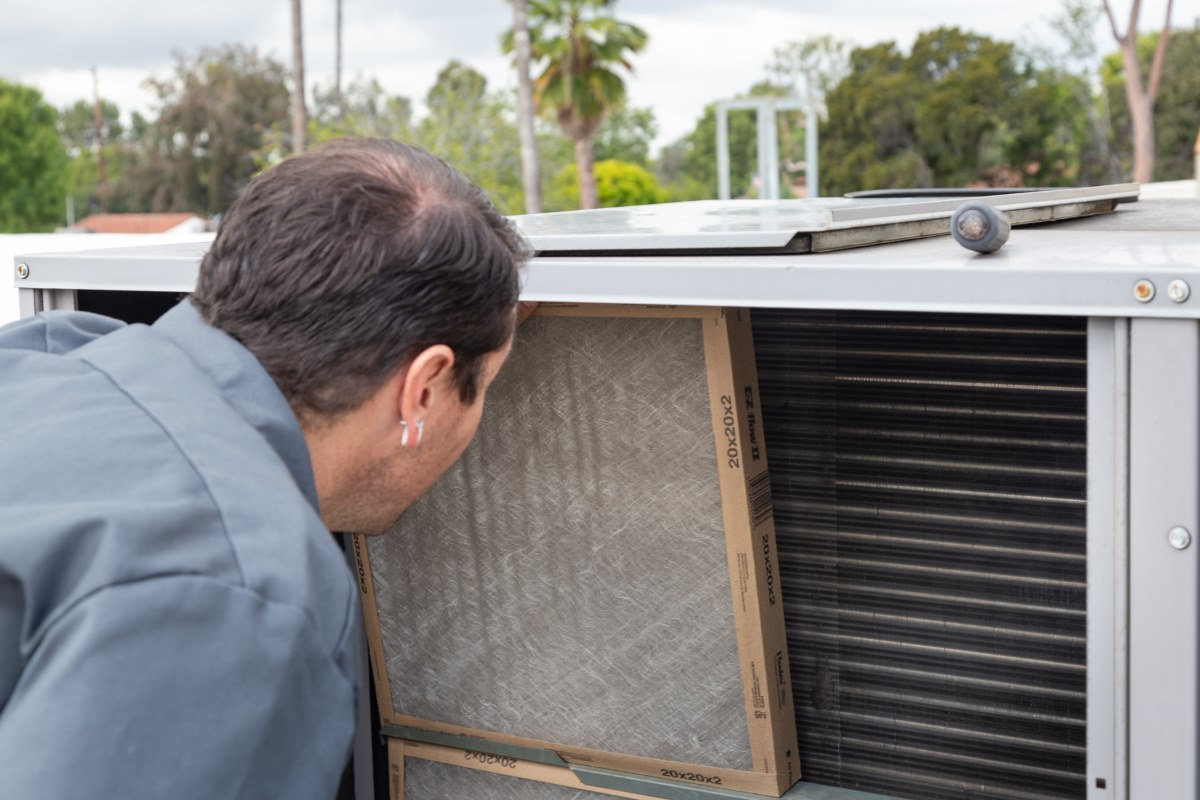 Technician inspecting the air filter inside an outdoor HVAC unit