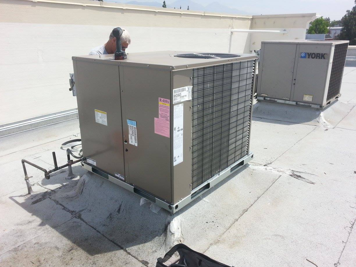 Rooftop HVAC unit and ducts on a flat roof, with power lines and industrial buildings in the background
