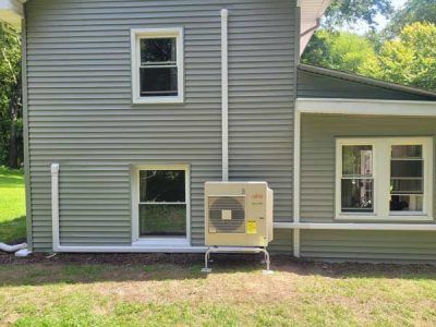 Rusty outdoor air conditioner unit with a fan on top, beside a wall and cables on the ground