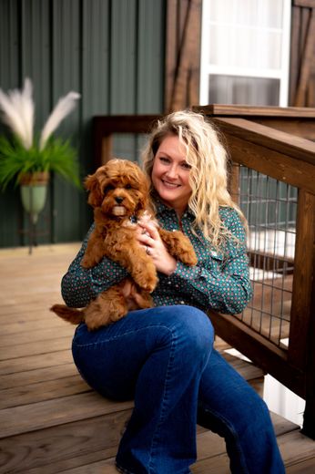 A woman is sitting on a deck holding a puppy.