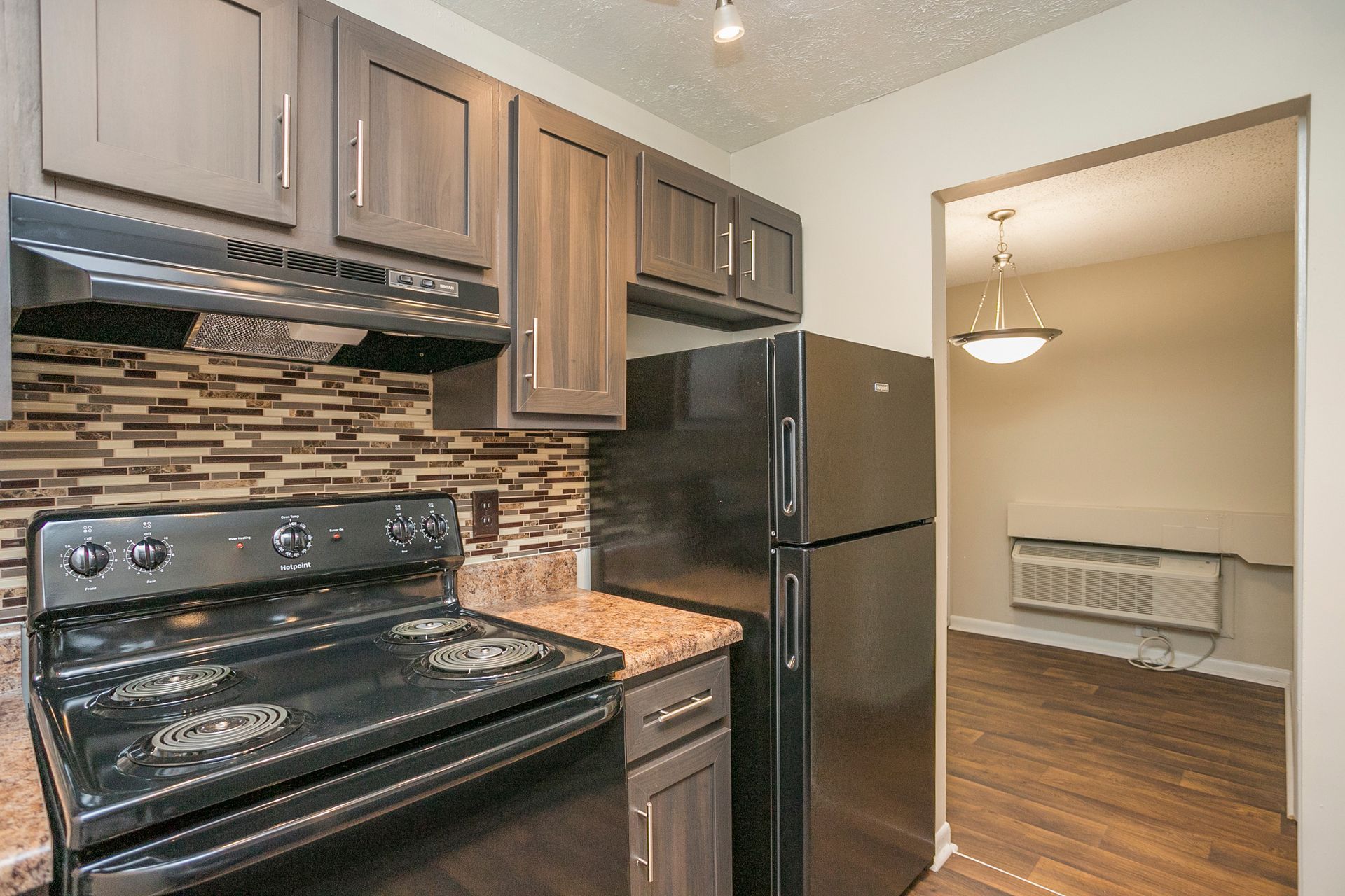 A kitchen featuring dark wood cabinets, a black stove, a black refrigerator, and a tiled backsplash, opening to a room.