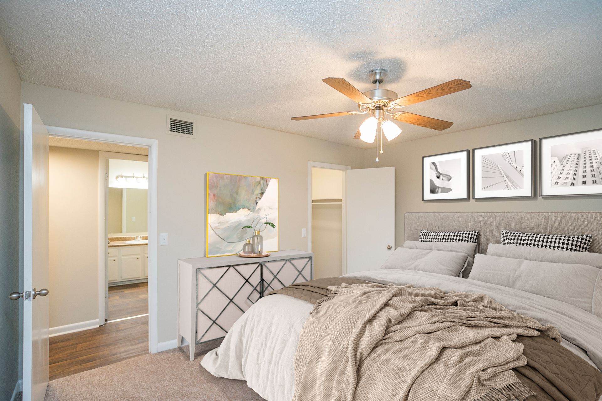 A bedroom with a king-sized bed, dresser, ceiling fan, and open doorways leading to a bathroom and closet.